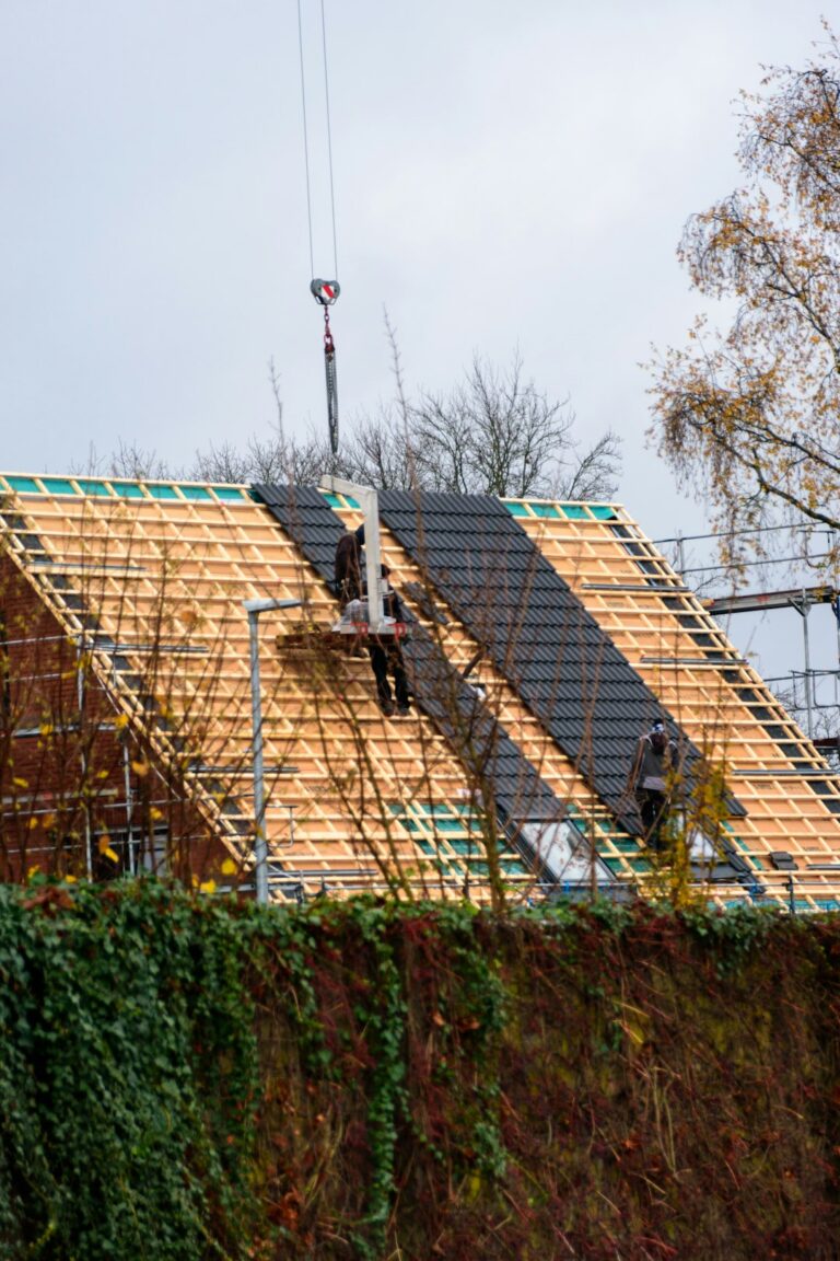 Workers secure a waterproof covering over an open roof section beside stacked lumber and renovation tools.