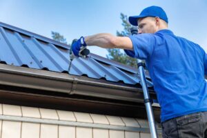 A homeowner examines loose shingles and damaged flashing beside a ladder on a residential roof.